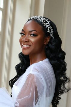 a woman wearing a bridal headpiece in front of a window smiling at the camera