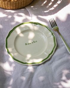 a white plate with green trim on it and a fork sitting next to the plate