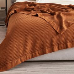 a bed with an orange blanket on top of it next to a night stand and lamp