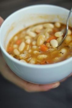 a person holding a bowl of soup with beans and carrots