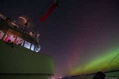 the aurora bore is visible in the night sky as people look on from a boat