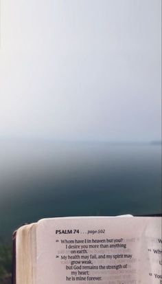 an open book sitting on top of a wooden table next to the ocean and sky