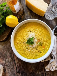 a bowl of soup with parmesan cheese and lemons next to it on a wooden table