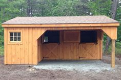 a large wooden shed with two doors and windows on the roof, in front of some trees