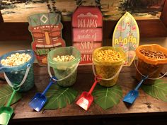 several buckets filled with food sitting on top of a wooden table next to surfboards