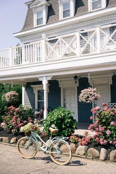 a bicycle parked in front of a house with flowers on the ground and bushes around it