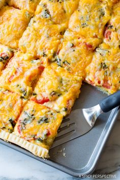 a pizza with cheese and spinach is on a baking sheet next to a spatula