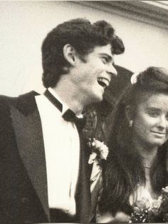 a man and woman standing next to each other in front of a building with flowers on their hair