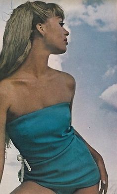 a woman in a blue one piece swimsuit with her hair blowing in the wind