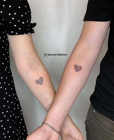 two people holding hands with small tattoos on their arms and hearts tattooed on the wrist