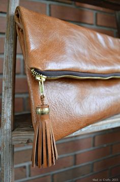 leather foldover clutch with tassels on a chair in front of a brick wall