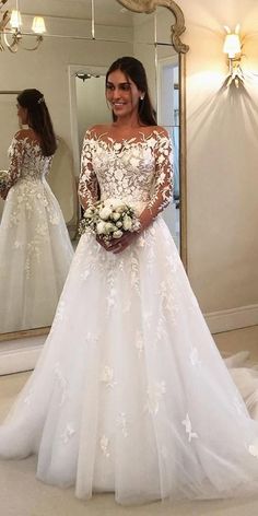 a woman standing in front of a mirror wearing a white wedding dress with long sleeves