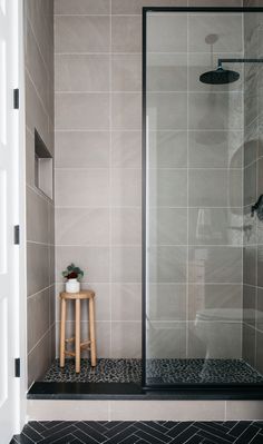 a walk in shower sitting next to a wooden stool on top of a tiled floor