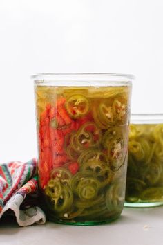 two jars filled with pickled vegetables on top of a white table next to each other