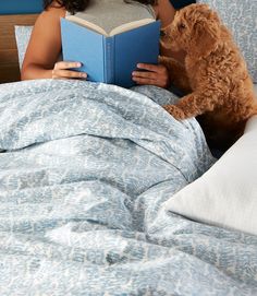 a woman reading a book in bed with her dog