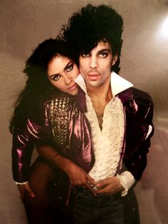 two people posing for a photo in front of a white wall with lights on it