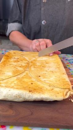 a person with a knife cutting into a piece of bread on top of a table