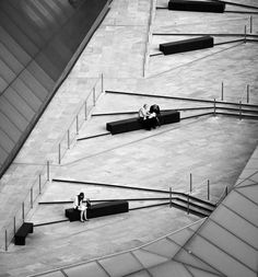 black and white photograph of people sitting on benches in an empty area with metal railings