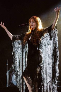 a woman in black dress standing on stage with her arms outstretched and legs spread out