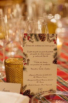 a place setting with wine glasses and pine cones on the napkins, next to an empty menu card