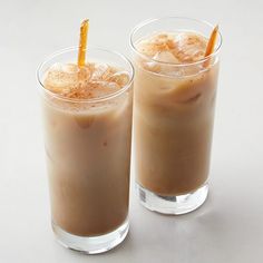 two glasses filled with iced coffee on top of a white table next to each other