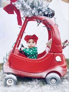 a baby in a red car with christmas decorations on top