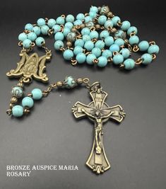 Measuring 20.25 inches long, this full 5 decade Rosary is made with 6mm howlite beads that were dyed to give the appearance of turquoise.  The Pater or Our Father beads are capped in bronze.; the center medal is called the Auspice Maria or Ave Maria Medal.  Cross and center Medal are both bronze as are the chains and joining loops.  The color of the beads really stands out with the bronze and gives the appearance of a heirloom rosary. Turquoise Rosary With Round Beads, Spiritual Turquoise Rosary With Round Beads, Rosary Beads Catholic, Decade Rosary, Meditation Beads, Our Father, Rosary Beads, Prayer Beads, Bead Caps