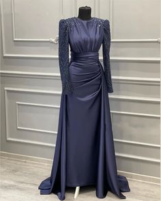 Elevate your evening elegance with our Exquisite Midnight Blue Gown, a perfect blend of timeless sophistication and modern glamour. Crafted from luxurious satin fabric, this gown features intricately embellished long sleeves adorned with delicate beadwork, adding a touch of shimmering magic to your look. The modest high neckline ensures a refined silhouette, while the pleated bodice accentuates your natural curves, offering a flattering fit thats ideal for formal occasions.The gowns unique design includes a meticulously draped waistband that gracefully complements the figure-hugging skirt. The subtle ruching and side drape create a flowing effect, allowing for ease of movement and a dramatic entrance wherever you go. A discreet back zipper ensures a seamless and elegant appearance from all Midnight Blue Gown, Navy Blue Evening Gown, Satin Evening Gown, Blue Evening Gowns, Celebrity Gowns, Long Sleeve Evening Gowns, Exquisite Gowns, Satin Evening Dresses, Blue Evening Dresses