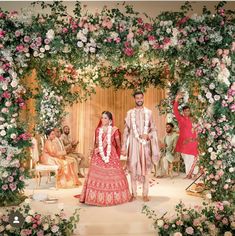 a man and woman standing in front of a flower covered stage with flowers all around them