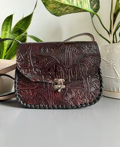 "Beautiful, burgundy and embossed with sunflowers, genuine leather hand tooled floral crossbody purse, skillfully made by Artisans in Mexico using the \"cincelada\" technique. Latch closure and adjustable tooled strap. Includes a storage bag to protect your purse when not in use. Dimensions: 9\" L x 3.5\" W x 7'' H. Please check measurements if you have any concerns about sizing before purchase. Imported from Mexico, they are a continuation of the fine craftsmanship established in that country going back hundreds of years with carved leather saddles. These beauties are not like the more common stamped products that can be mass produced cheaply and sold. Each piece is hand-cut by skilled artisans in leather carving, preserving the art and tradition of a centuries old technique which is stil Sunflower Purse, Handbags Handmade, Tooled Leather Purse, Floral Handbags, Leather Carving, Wardrobe Style, Leather Tooling, Crossbody Purse, Slow Fashion