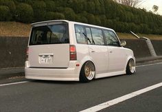 a white minivan parked on the side of a road next to a fence and bushes