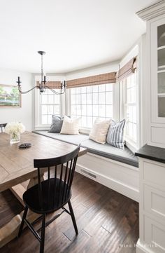 a dining room table with two chairs and a bench in front of the bay window