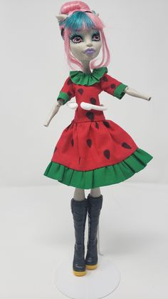 a doll with pink hair wearing a red dress and green polka dot print skirt, black boots