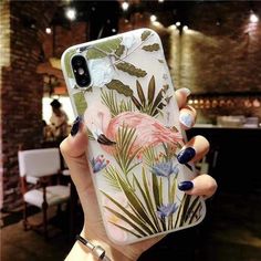 a woman holding up her phone case with flamingos and tropical leaves on the back