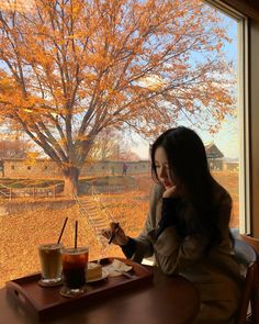 a woman sitting at a table in front of a window looking at her cell phone