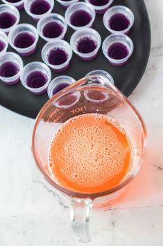 a blender filled with orange juice next to a tray of purple jellies