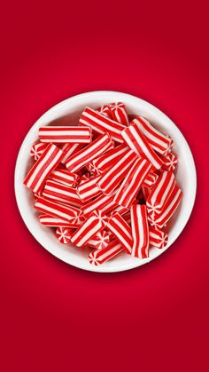 red and white striped candy canes in a bowl on a red tablecloth background