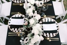 a black and white table setting with place settings, napkins and flowers on it