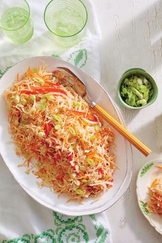 a white plate topped with coleslaw next to two bowls of vegetables and chopsticks