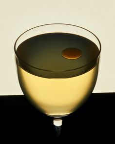 a glass filled with white wine sitting on top of a black table next to a wall