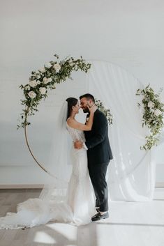 a bride and groom standing in front of a floral arch