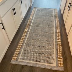 a kitchen with white cabinets and wooden flooring next to a rug on the floor