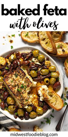 baked feta with olives in a white bowl on a marble counter top next to bread