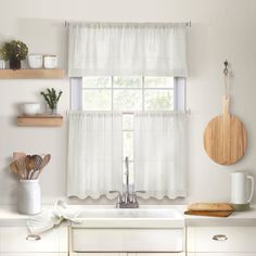 a kitchen with white curtains and wooden utensils on the window sill above the sink