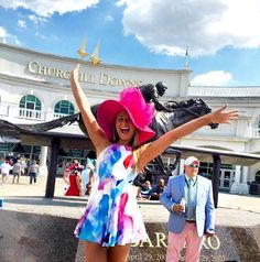 a woman in a colorful dress and pink hat posing for the camera with her arms outstretched