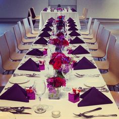 a long table with purple and red flowers on it is set for a formal dinner