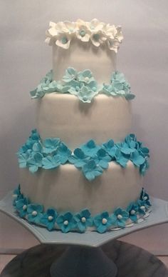 a three tiered cake with blue and white flowers on it's side, sitting on a platter