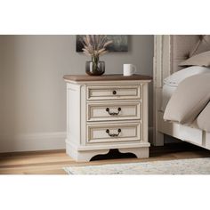 a white nightstand with two drawers and a vase on it next to a bed in a bedroom