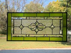 a green stained glass window hanging in front of a house with trees and grass behind it