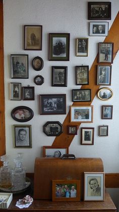 a wall with many framed photos and pictures on it, along with a wooden table